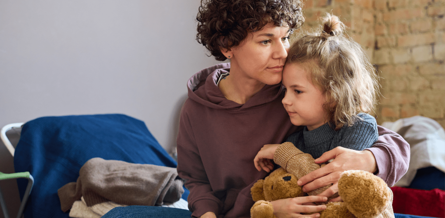 mother and daughter embracing eachother. daughter is holding a teddy bear